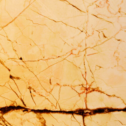a close-up of a natural stone with a golden-yellow base color, featuring intricate patterns of white, grey, and black veins, and a polished surface with a slight shine.