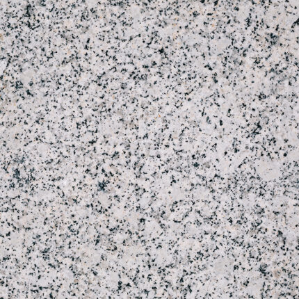 A white granite slab with grey and black speckles and patches.