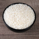 The image may show a bowl of cooked Ambemohar rice or a pile of uncooked rice grains. Ambemohar rice is known for its distinctive aroma, reminiscent of mango blossoms (Ambemohar translates to 