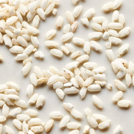 Arborio rice grains are medium in size and have a pearly white color. The image may show a pile of uncooked Arborio rice grains or a cooked dish of creamy risotto made with Arborio rice.
