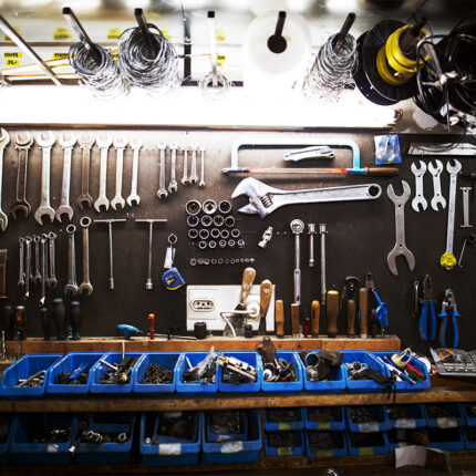 The tools include wrenches, sockets, pliers, screwdrivers, hammers, and other hand tools. The tools are laid out neatly on a workbench, with some tools hanging on a pegboard in the background.