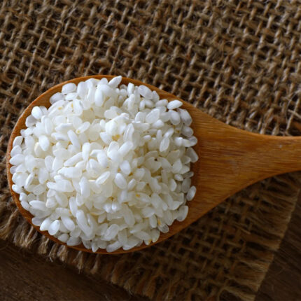 The image may show a bowl of cooked sushi rice or a pile of uncooked rice grains. Sushi rice is specifically prepared with a combination of vinegar, sugar, and salt to achieve a sticky yet slightly tangy flavor.