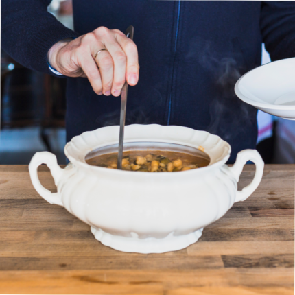 A ceramic soup tureen with lid and ladle, filled with delicious and steaming soup.